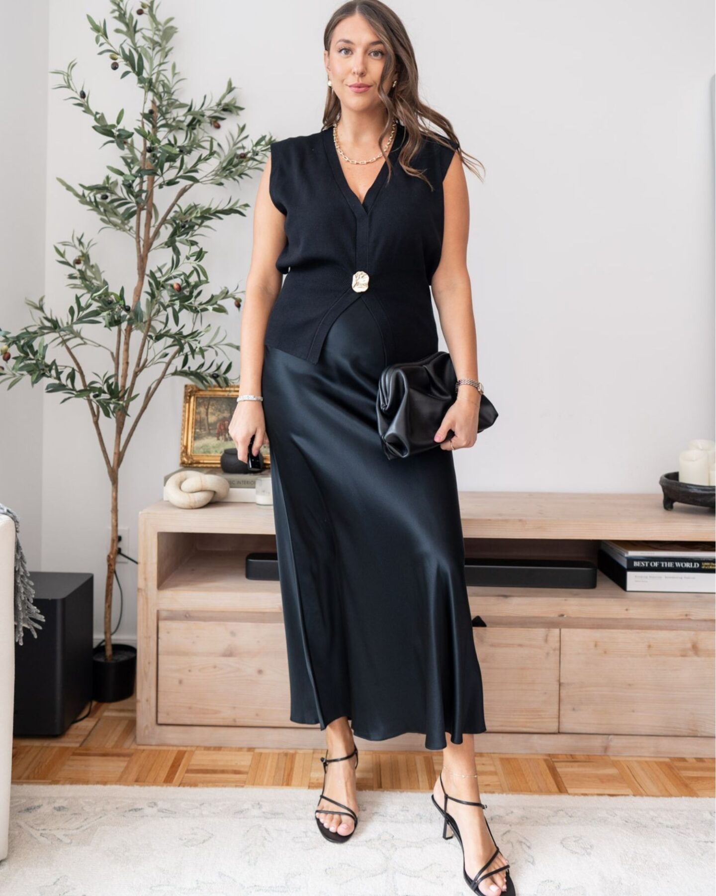 Woman wearing black sleeveless statement button vest styled with satin midi skirt and heels