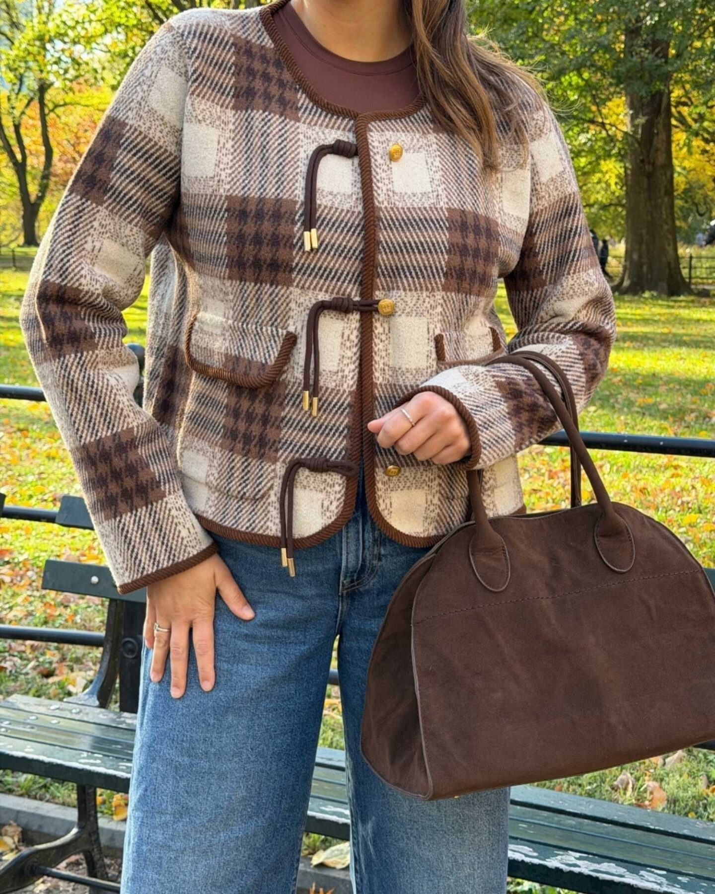 Woman wearing a brown plaid fall jacket with jeans in a park