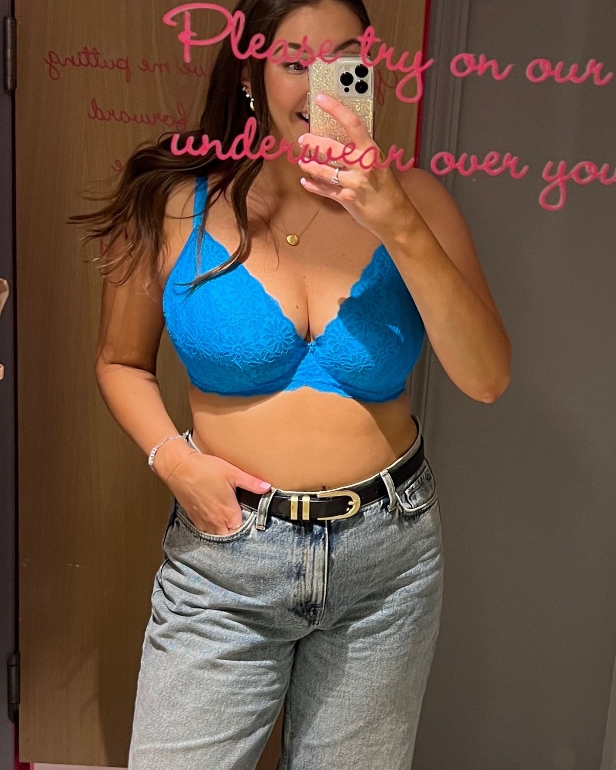 Woman with a fuller bust trying on a supportive blue underwire bra in a fitting room mirror